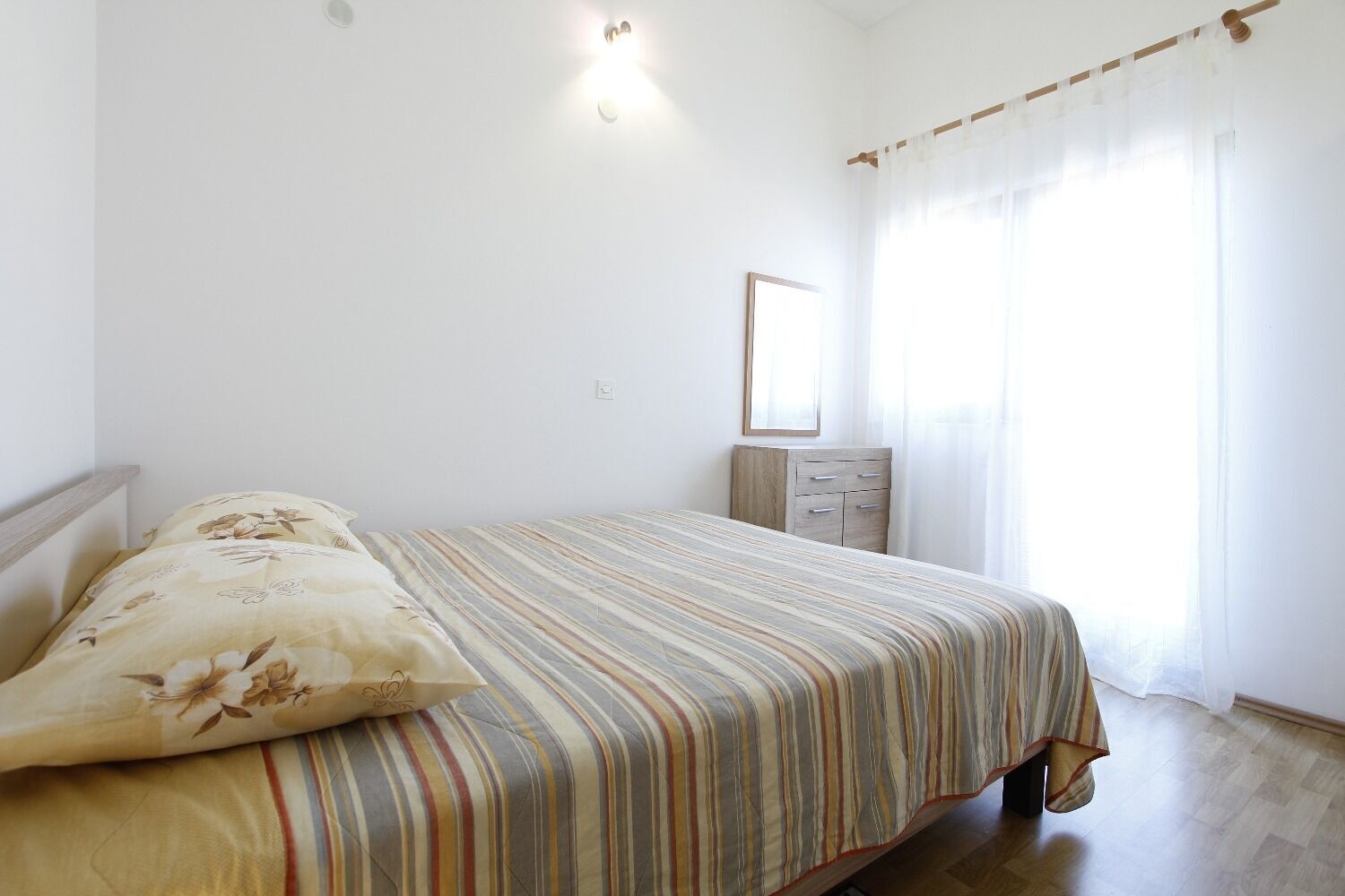 Een slaapkamer met een bed, nachtkastje, dressoir en een spiegel.
