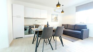 Una cocina moderna con armarios blancos, una mesa de comedor con sillas y un sofá gris en la sala de estar.