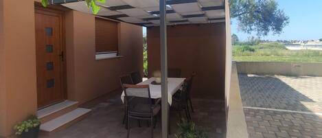 A covered patio area with a table and chairs, a small plant, and a door with a window.