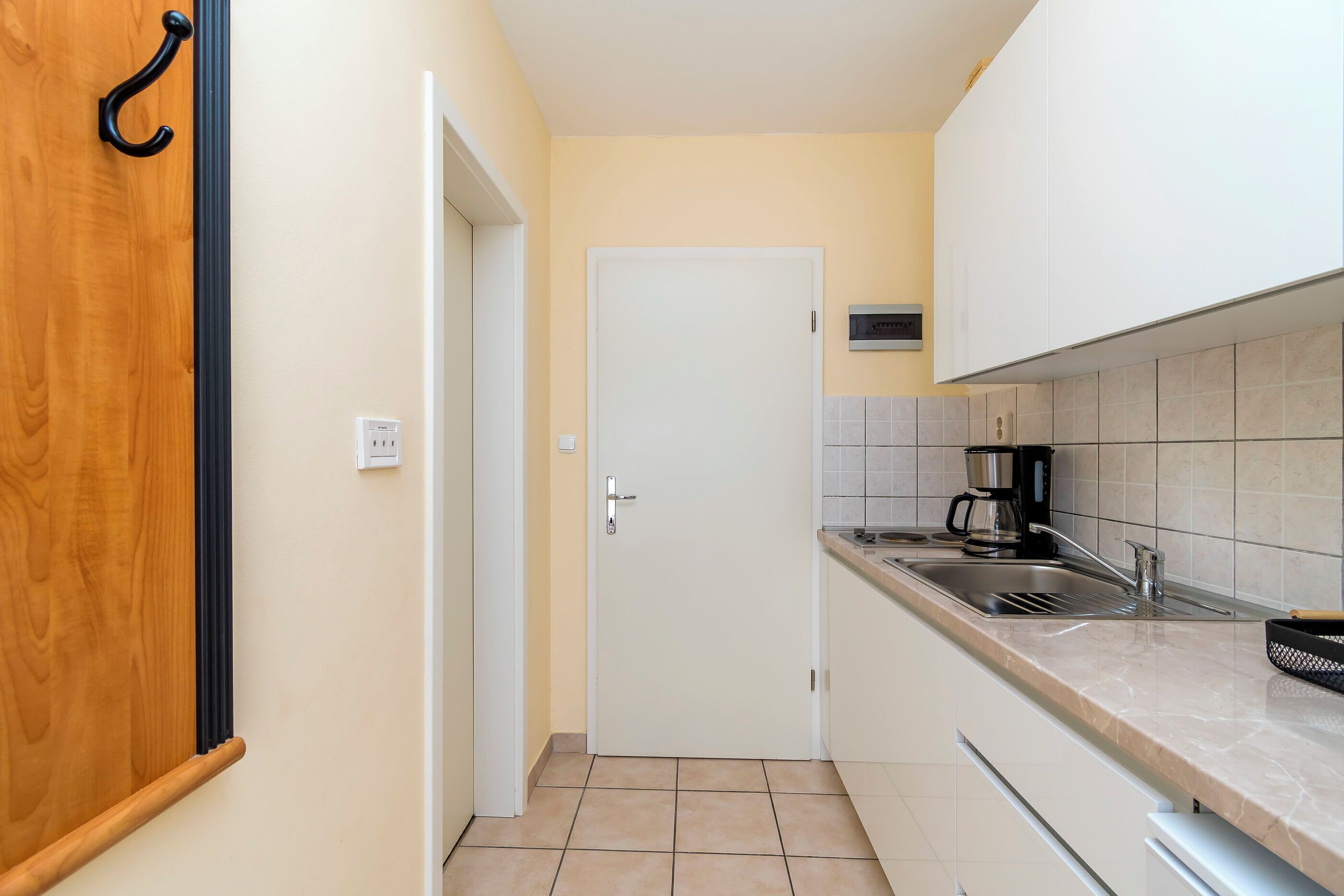 Una cucina compatta con una porta bianca, una macchina da caffè e un lavandino.