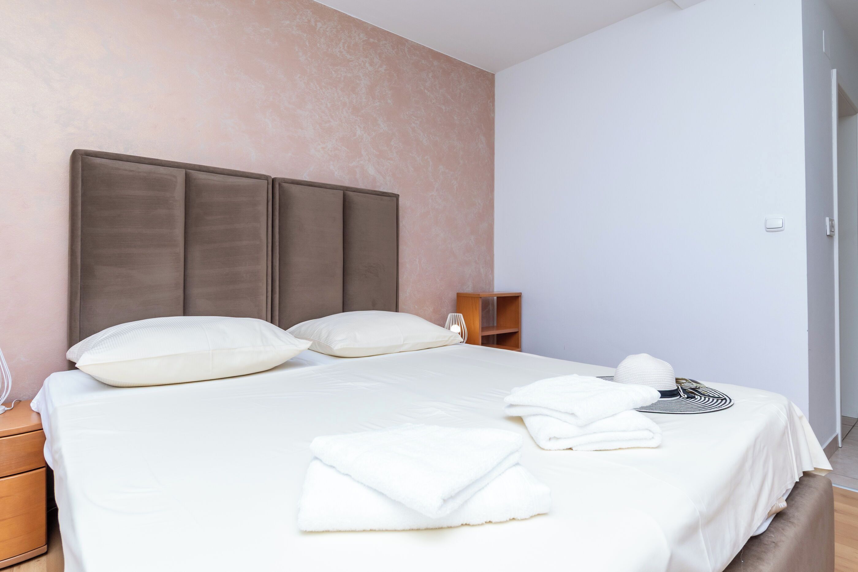 A neatly made bed with pillows, a bedside table with a lamp, and a small wooden nightstand.