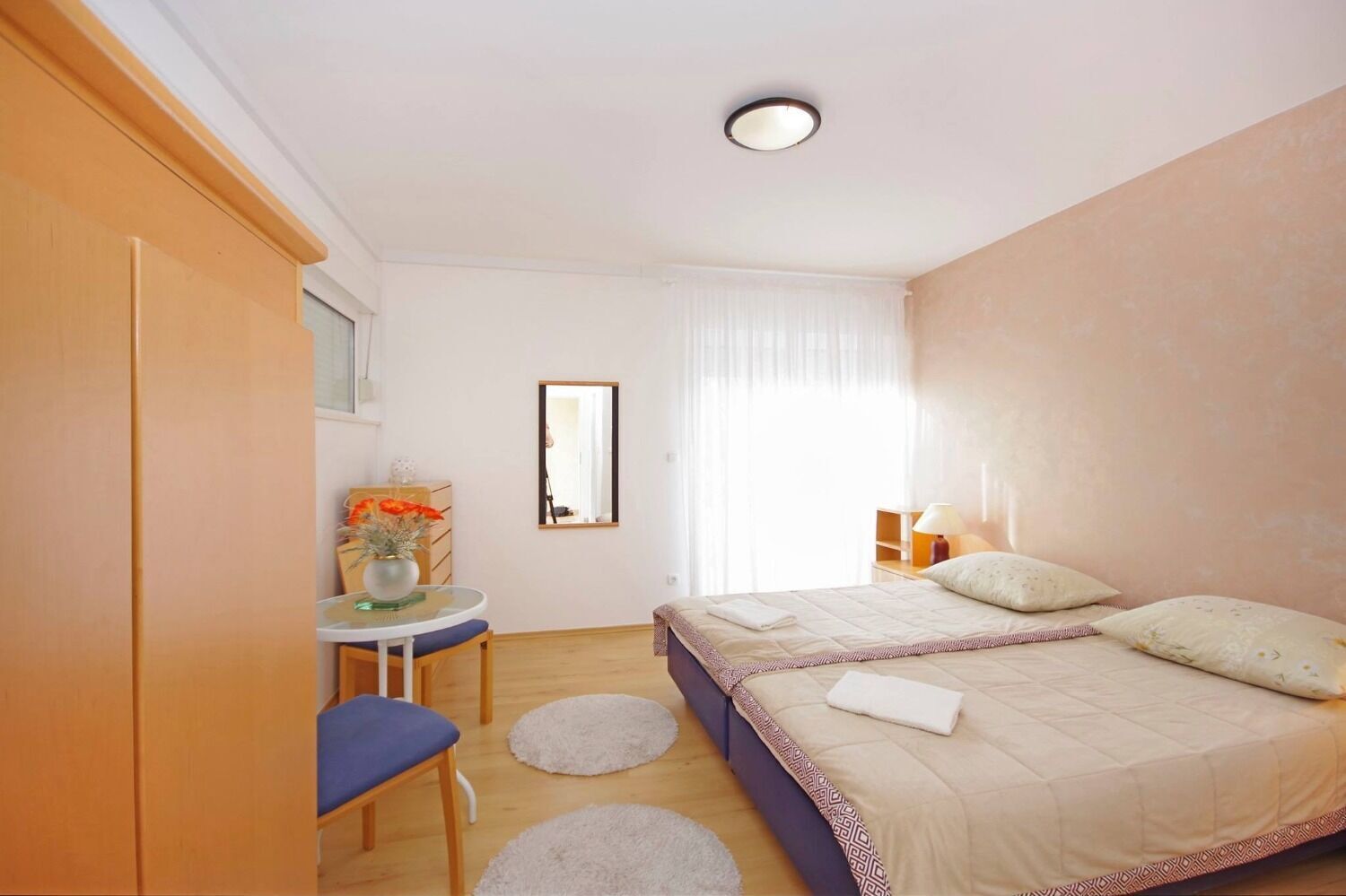 Quarto com cama, mesa de cabeceira, cadeira e uma pequena mesa com um vaso de flores.
