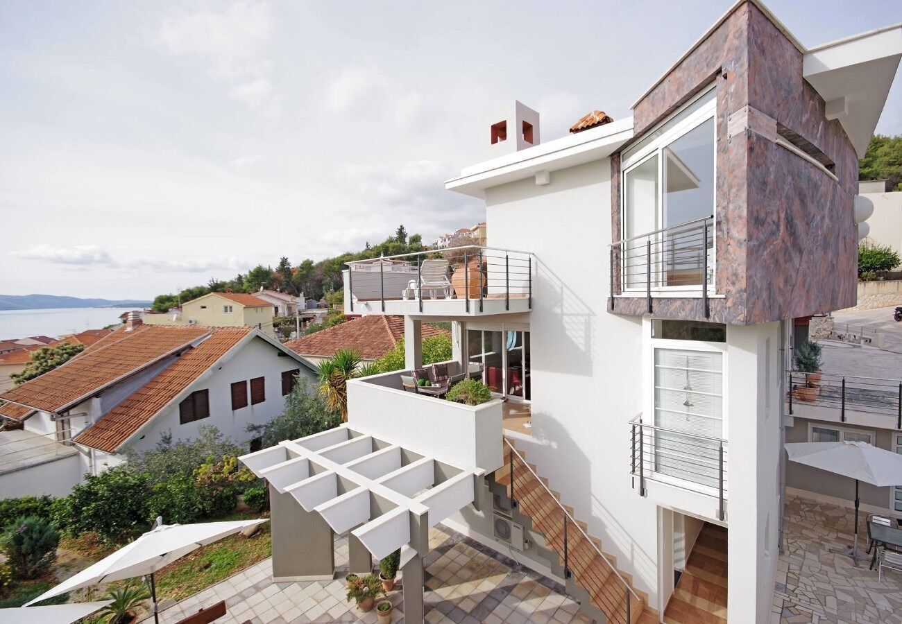 Una casa moderna a due piani con un balcone, area salotto esterna e vista sul mare.
