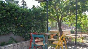 Un'area salotto all'aperto con tavolo e sedie, immersa nel verde e circondata da un muro in pietra.