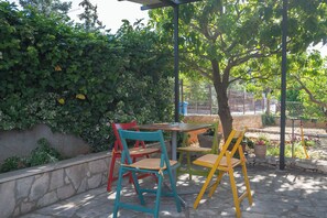 An outdoor seating area with a table and chairs, surrounded by greenery and a stone wall. - Apartment Sani (Supetar)