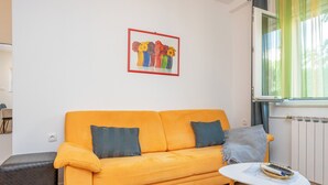 Una stanza con un divano giallo, un tavolino, un termosifone e una finestra con tende.