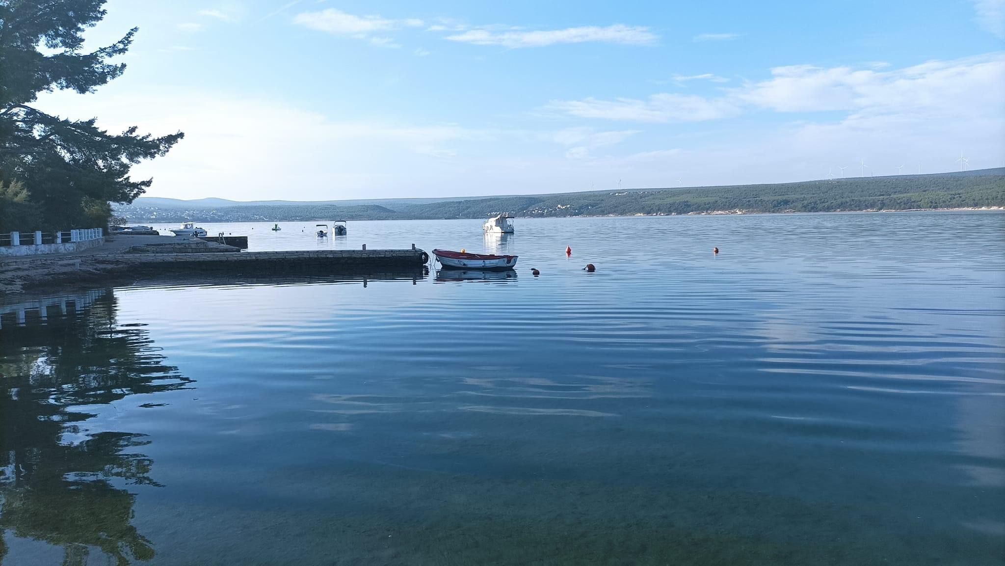 A calm lake with boats, a dock, and distant wind turbines.
