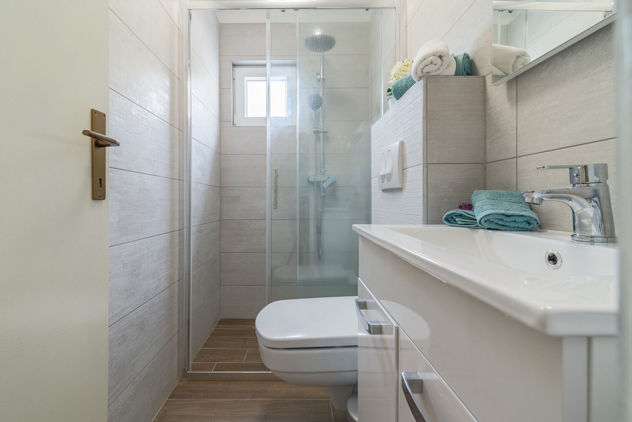 Un baño moderno con ducha envuelta en vidrio, inodoro blanco y lavamanos con espejo.