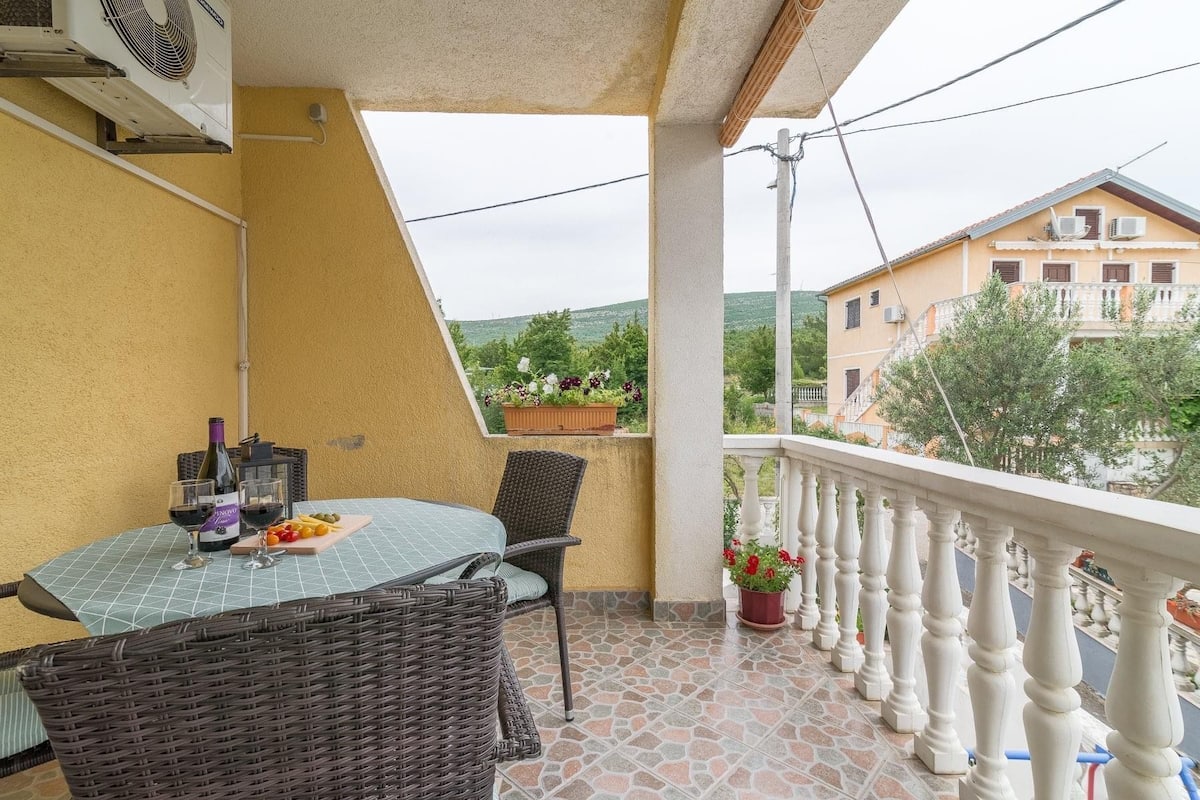 A balcony with a table, chairs, a bottle of wine, and a potted plant.