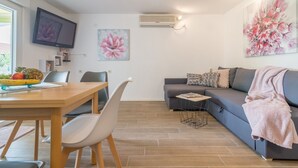 A modern living room with a sofa, a dining table with chairs, a flat-screen TV, and artwork on the walls. - Apartments Sandra (Obrovac)
