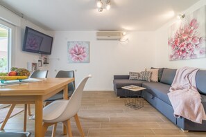 Ein modernes Wohnzimmer mit einer Couch, einem Esstisch mit Stühlen, einem Flachbildfernseher und Kunstwerken an den Wänden.