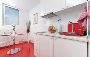 A modern kitchen with white cabinets, a red countertop, and a window with a white flower vase. - Apartment Asja (Zagreb)