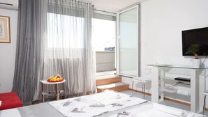 A modern hotel room with a large window, a flat-screen TV, a glass coffee table with fruits, and a neatly made bed. - Apartment Asja (Zagreb)