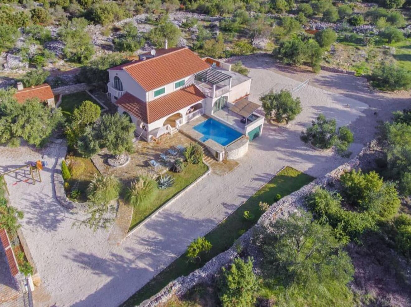 Une maison à deux étages avec une piscine, entourée d’un jardin aménagé et d’une allée gravillonnée.