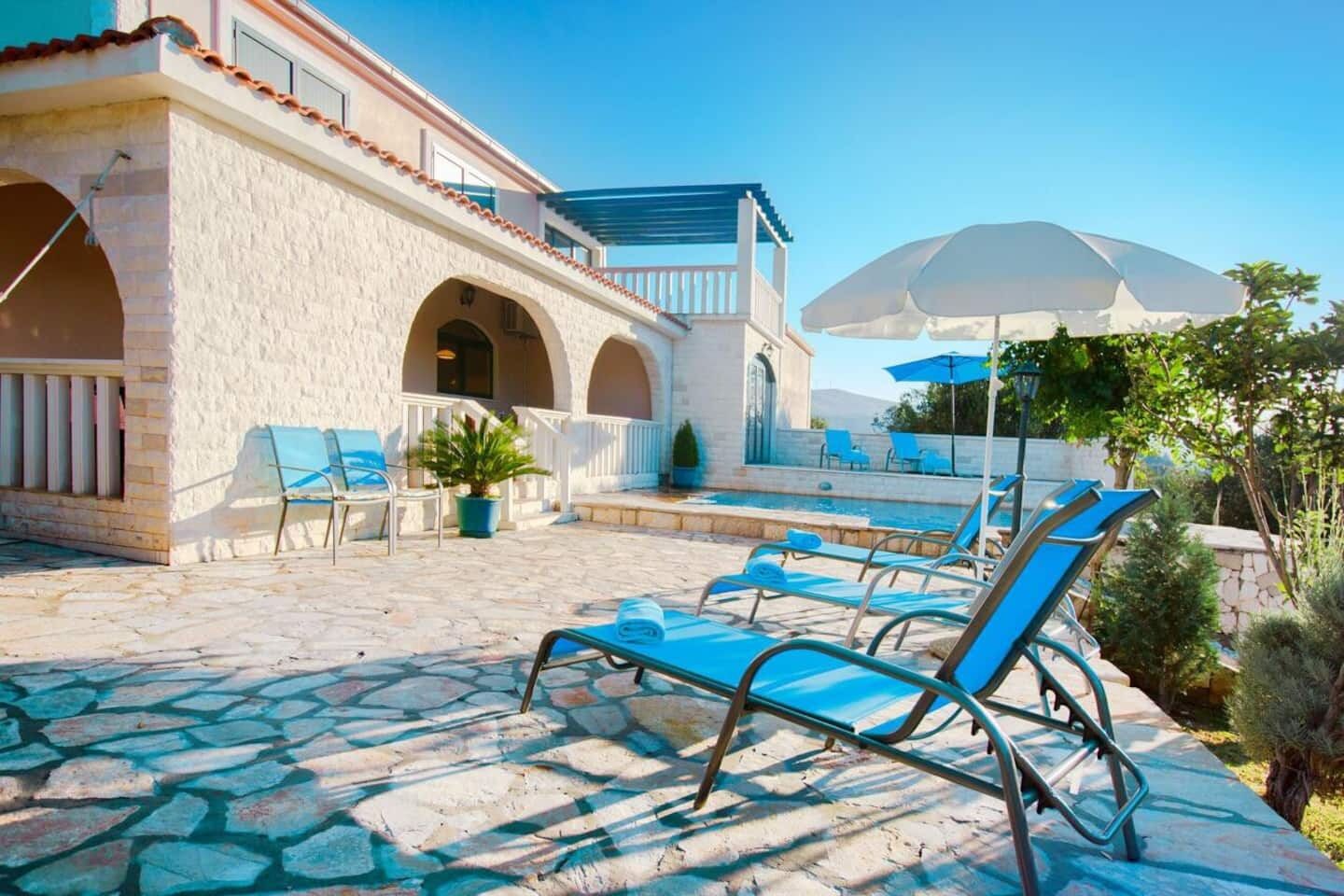 A pool area with lounge chairs, a pergola, and a stone patio.