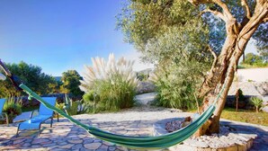 A hammock tied between two trees in a stone-paved garden with a clear sky. - House Stone&olive (Marina)