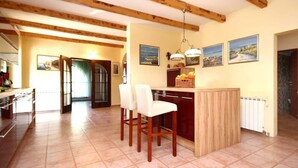 A spacious kitchen with wooden beams, a central island with bar stools, and a dining area with a view of the outdoors. - House Stone&olive (Marina)