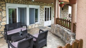 Une terrasse extérieure avec des meubles en osier, des murs en pierre et une clôture en bois.