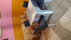 A dining area with a table and chairs, a patterned tablecloth, and a wooden floor. - Apartments Lukovac (Blato)