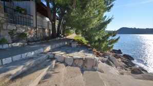 A stone pathway leading to a waterfront property with a stone wall and a view of the sea. - Apartments Lukovac (Blato)