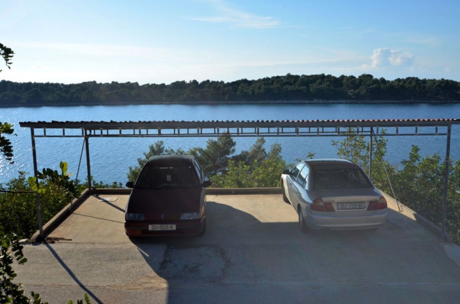 Two cars parked in a covered parking area with a view of a lake and trees in the background.