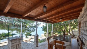A covered outdoor area with stone flooring, a wooden table, and benches. - Apartments Lukovac (Blato)