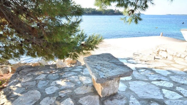 A stone bench overlooking a body of water with a clear view of the shoreline. - Apartments Lukovac (Blato)