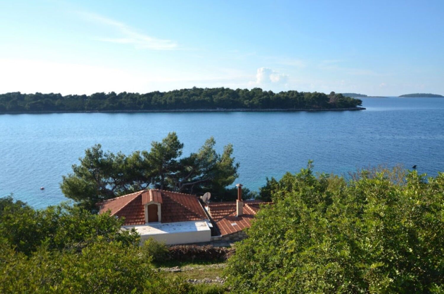 A house with a red roof, surrounded by greenery and overlooking a large body of water.