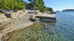 A stone staircase leading to a dock by a clear lake, with boats moored nearby and trees in the background. - Apartments Lukovac (Blato)