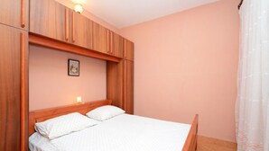 A bedroom with a wooden bed frame, two pillows, a nightstand with a lamp, and a framed picture on the wall. - Apartments Lukovac (Blato)