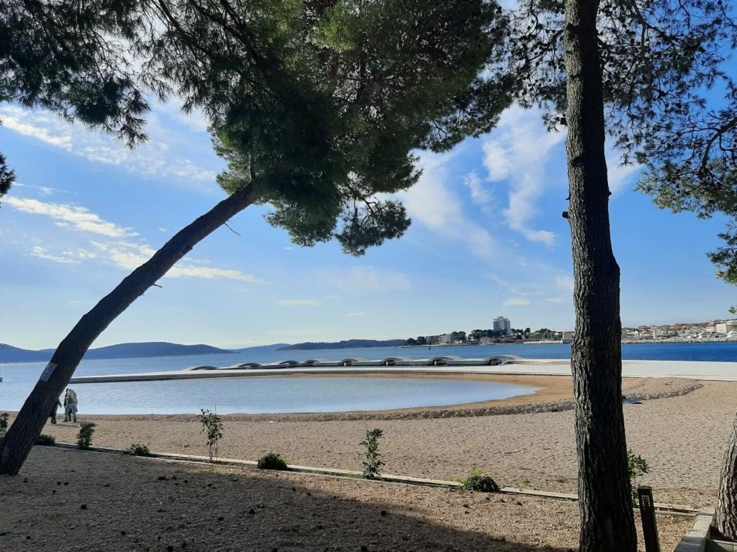 A beach with a clear view of the sea, a distant building, and a few trees.