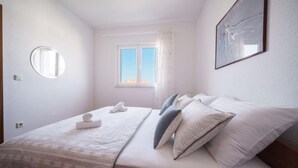 A bedroom with a bed, pillows, a window, and a mirror. - Apartments Josip (Vodice)