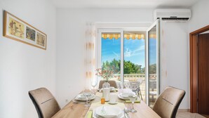 A dining area with a wooden table set for four, chairs, and a view through a glass door to an outdoor area with a table and chairs. - Apartments Josip (Vodice)