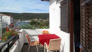 Un balcone con tavolo e sedie, affacciato su una zona costiera con case e barche.