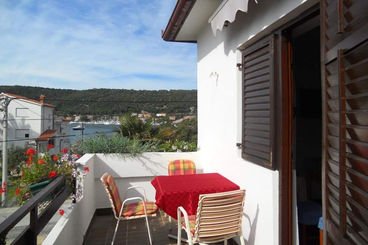 A balcony with a table and chairs, overlooking a coastal area with houses and boats.