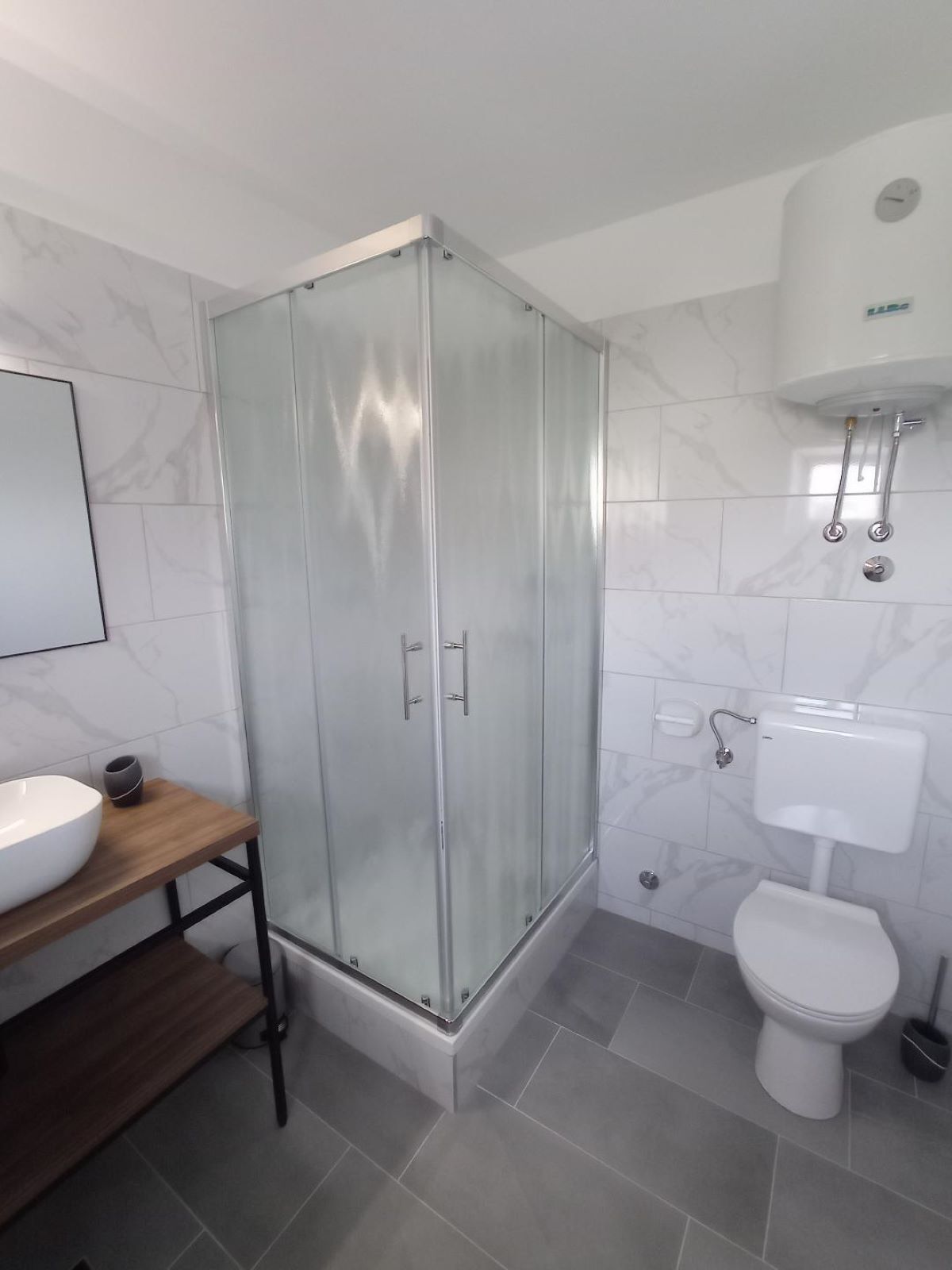 Un baño moderno con ducha de vidrio, lavamanos blanco y retrete.