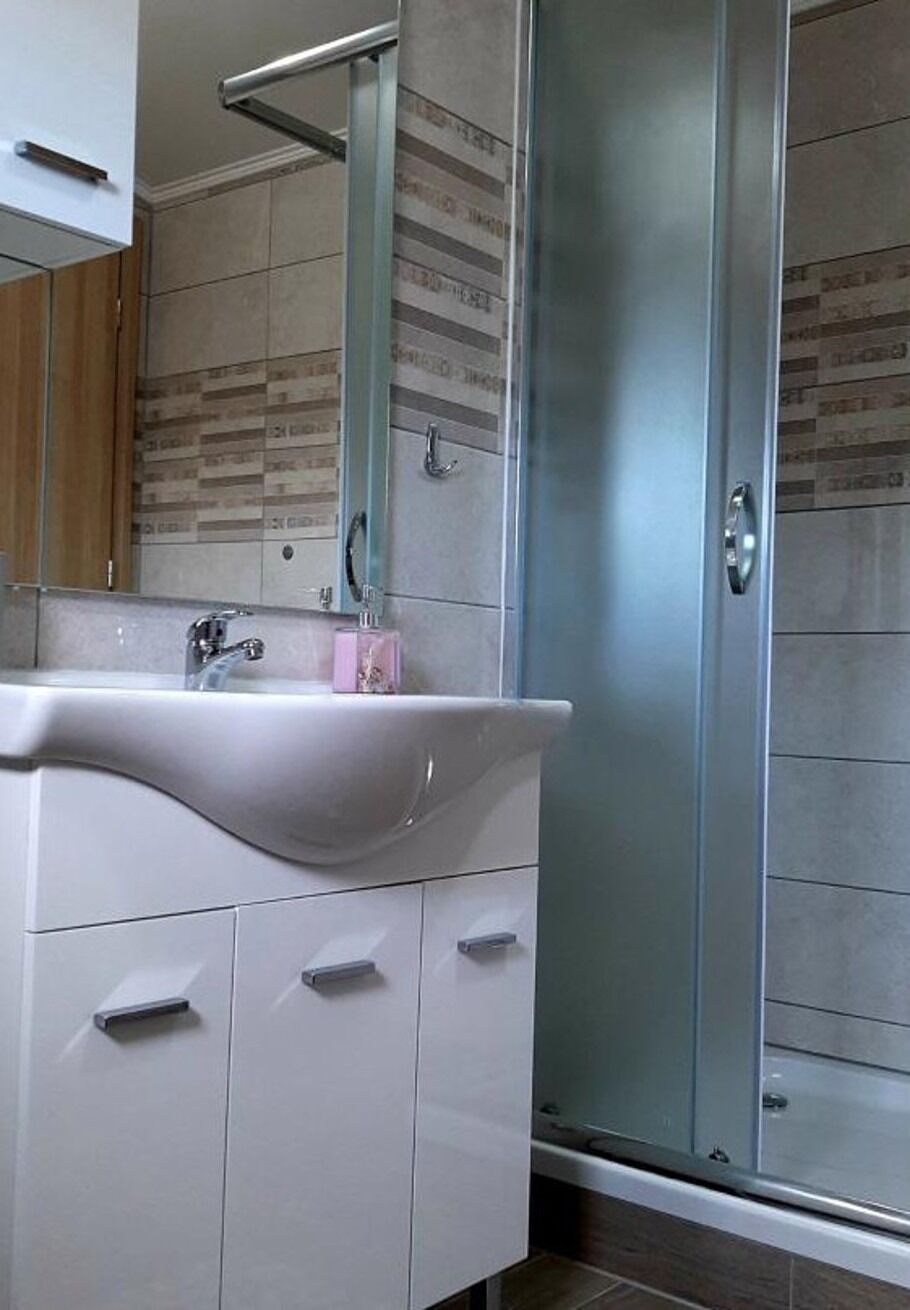 A bathroom with a white vanity, a sink, a mirror, and a glass shower enclosure.