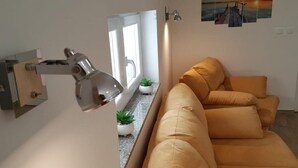 A modern living room with a sofa, a wall-mounted lamp, and a window with a view of the outside. - Apartment Sime (Vrsi)