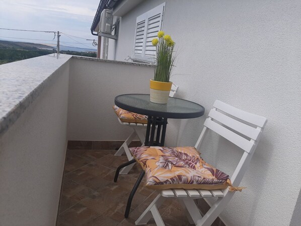 Ein kleiner Balkon mit einem runden Tisch, einem weißen Stuhl, einem Blumentopf und Blick auf die Landschaft.