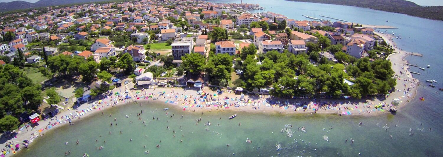 An aerial view of a coastal town with a beach, houses, and boats.
