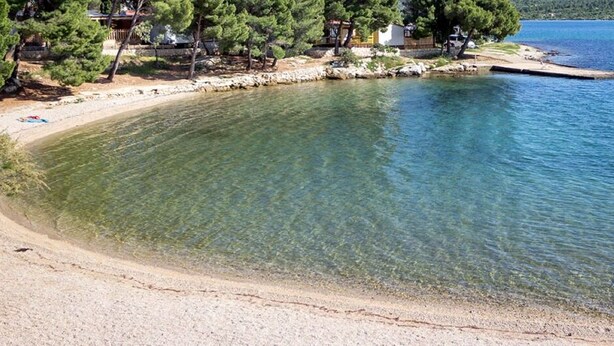 A clear lake with a sandy beach, trees, and a dock. - Apartment Maria (Pirovac)