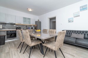 A modern kitchen with a dining area, grey sofa, and artwork on the wall. - Apartment Lilac (Trogir)