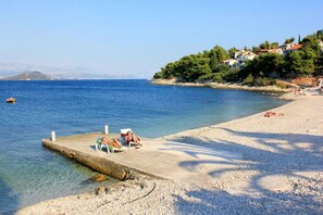 A beach with a pier, clear water, and a hillside with buildings. - Apartment Lilac (Trogir)
