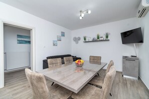 A modern dining area with a wooden table, cushioned chairs, and a fruit bowl centerpiece. - Apartment Lilac (Trogir)