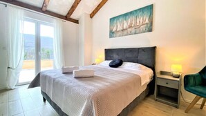 Ein Schlafzimmer mit einem großen Bett, einem Nachttisch mit Lampe, einem Sessel und einem Gemälde von Segelbooten an der Wand.