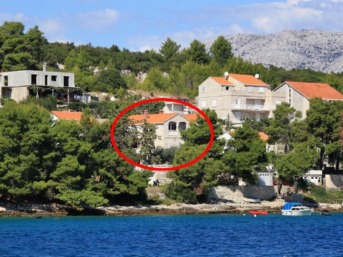 Un edificio costero con fachada de piedra, rodeado de árboles y un mar azul cristalino.