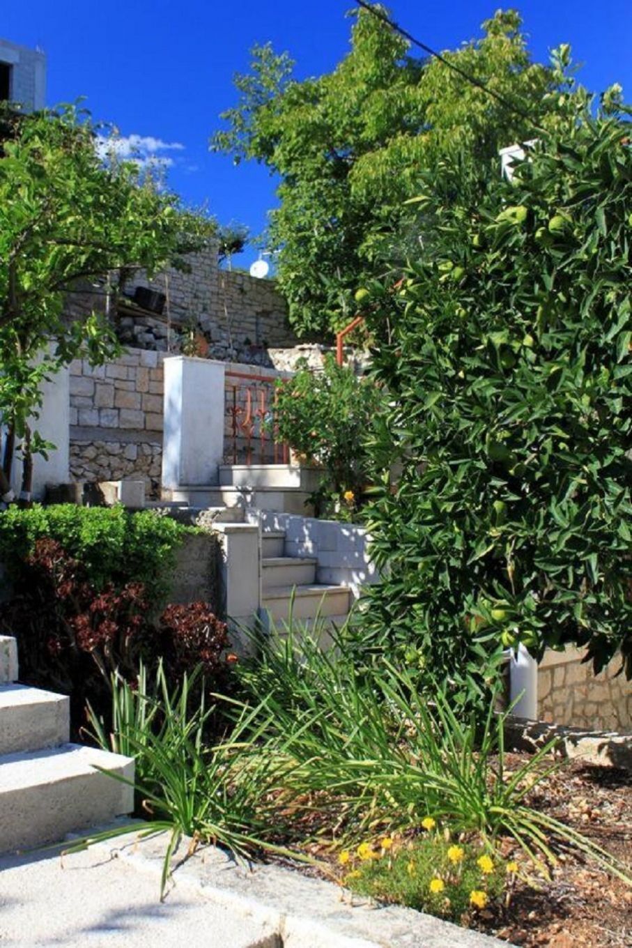 A stone building with steps leading up to a door, surrounded by greenery and a clear blue sky.