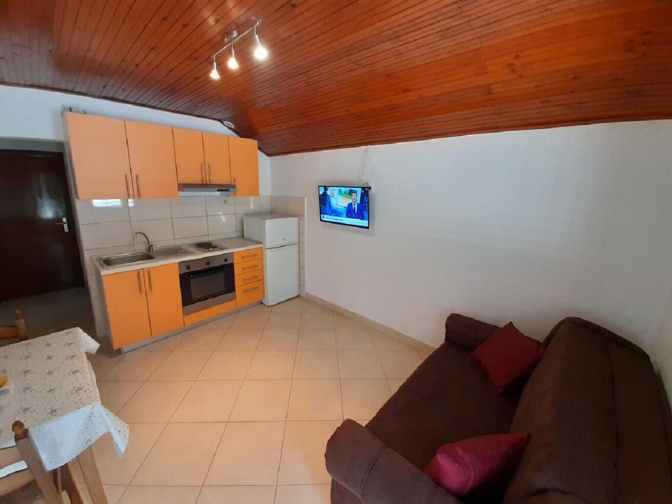 A compact living space with a kitchenette, a brown sofa, and a television mounted on the wall.