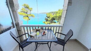 Un balcon avec une table et deux chaises, offrant une vue panoramique sur la mer et la végétation.
