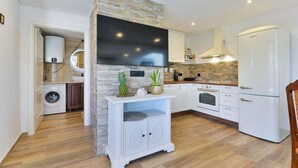 Una cucina moderna con mobili bianchi, forno integrato, microonde e un grande schermo piatto a parete.